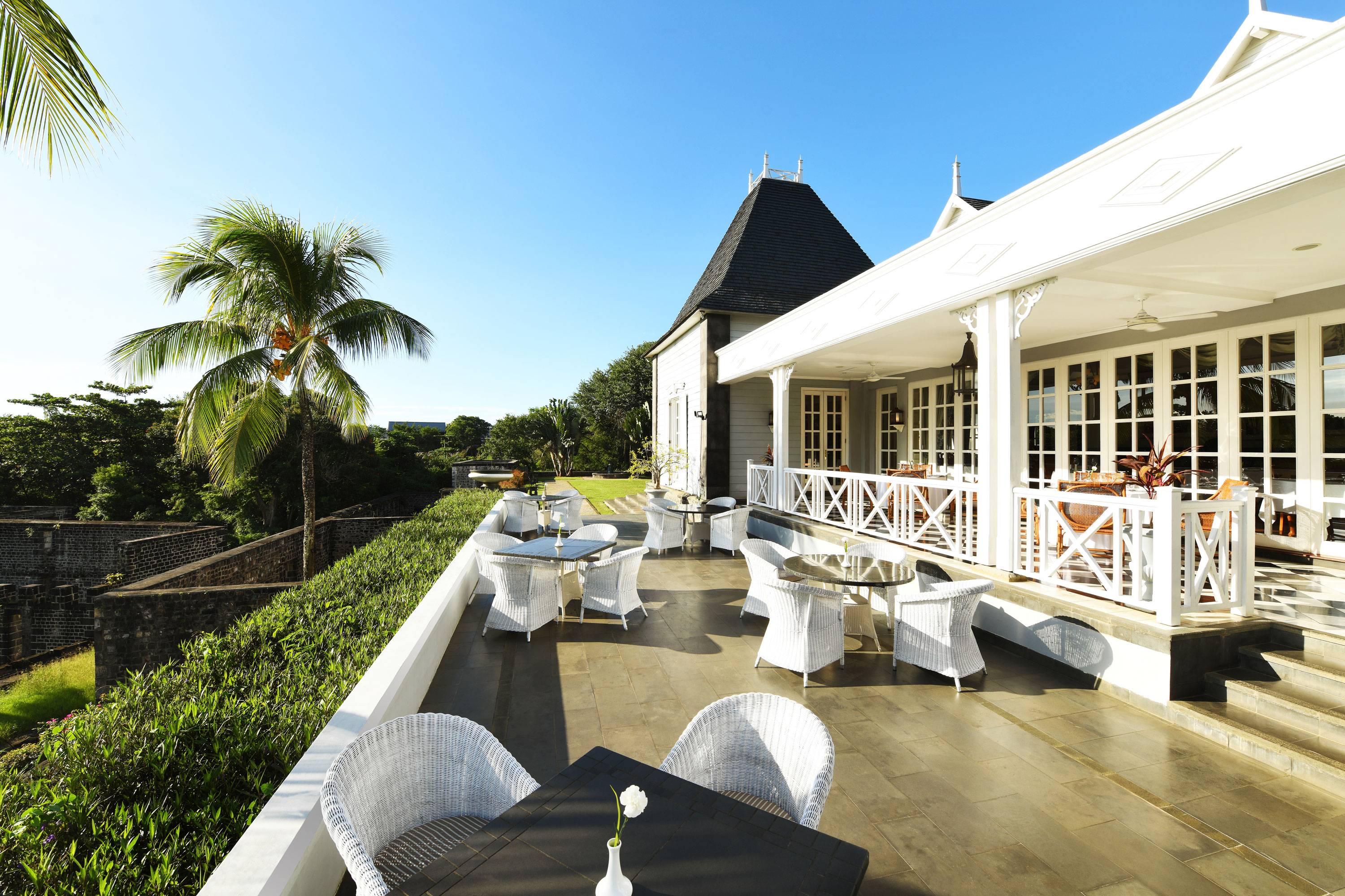 Eventlocation "Château Mon Désir" Terrasse mit stilvollen Rattanmöbeln, Blick auf den Garten und das Gebäude im Hintergrund
